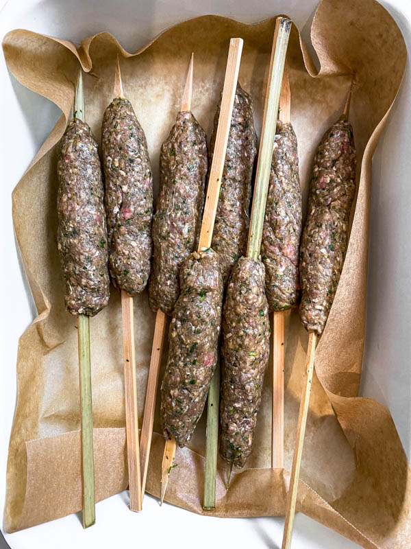 Looking down onto a tray of shaped kofta skewers.