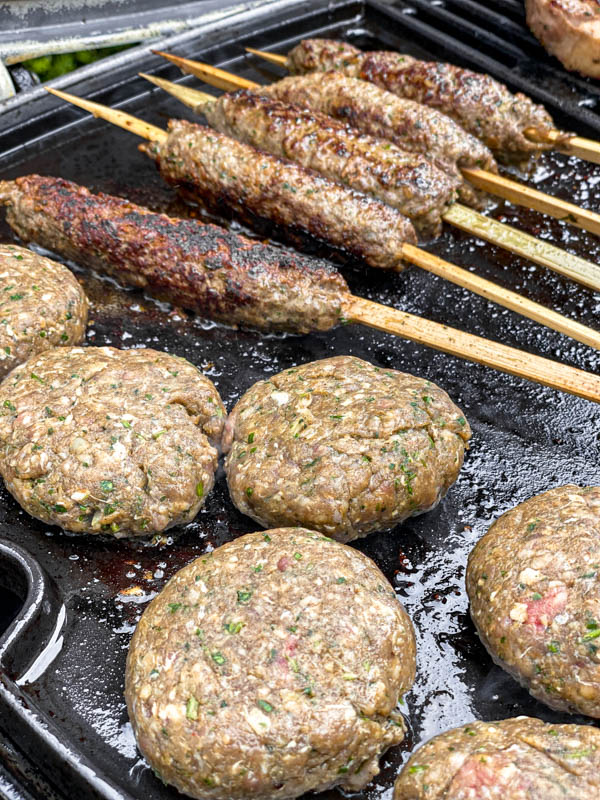 The kofta skewers and patties are cooking on a barbeque plate.