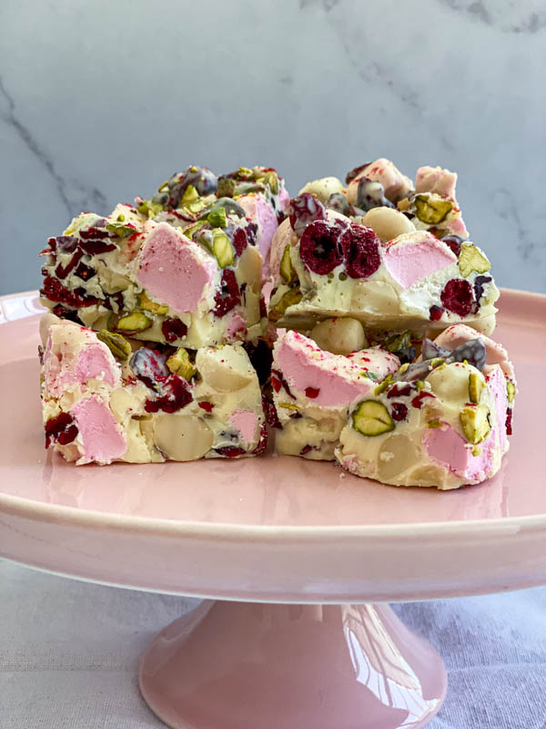 Squares of White Chocolate Rocky Road are placed on top of a pink cake stand.