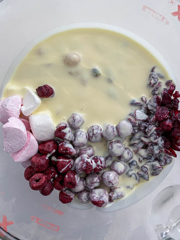 The melted white chocolate has been poured over the nuts, cranberries, marshmallows and freeze-dried cherries in the bowl.