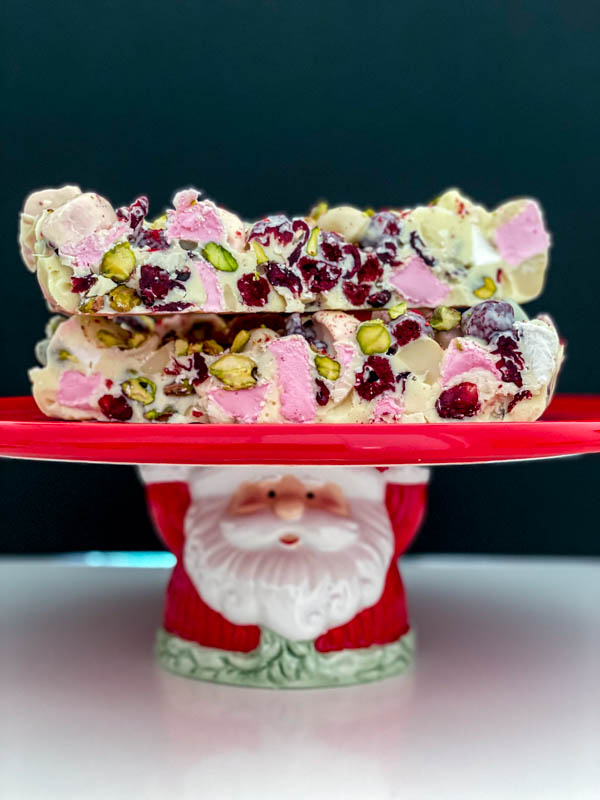 Slices of White Chocolate Rocky Road are on a red Santa pedestal cake stand.