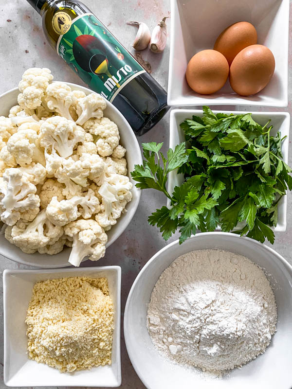 All the ingredients are shown here to make these Cauliflower Fritters. There are cauliflower florets, parsley, eggs, parmesan cheese, self raising flour, garlic and olive oil.