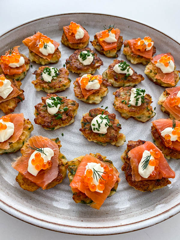 A platter of fritters are topped with smoked salmon, sour cream and salmon roe. Others are topped with sour cream and chives.