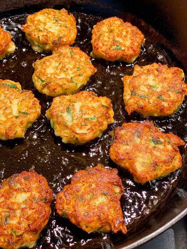 A close up of the fritters cooking in a frying pan. They are golden in colour and are bite sized.