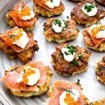 The fritters are on a large round platter. Some are topped with smoked salmon slices with a dollop of sour cream, salmon roe and dill. Others are topped with just sour cream and chives.