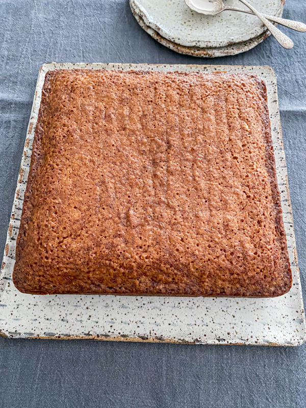 The cake is on a square serving plate on a table with cake plates and spoons in the background.