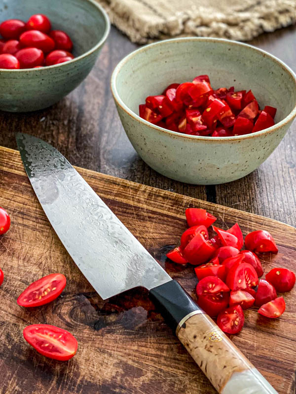 The tomatoes are being sliced here on a chopping board. They are being cut into small pieces.