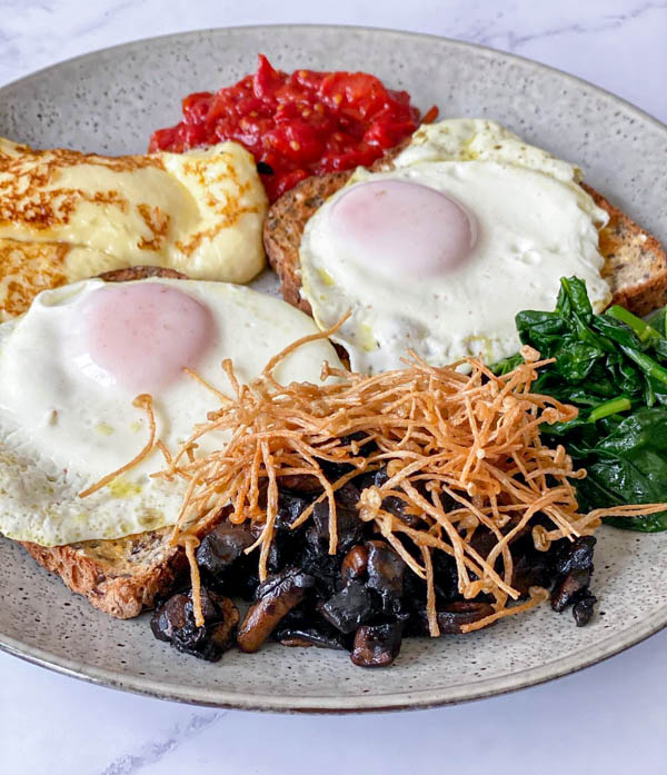 A cooked breakfast on a plate with some breakfast tomatoes.