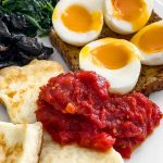 A close up of the Breakfast Tomatoes on a plate with Halloumi, boiled eggs, mushrooms and spinach.