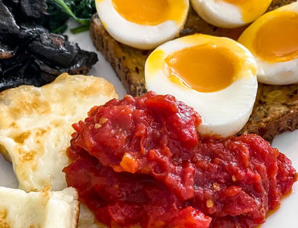 A close up of the Breakfast Tomatoes on a plate with Halloumi, boiled eggs, mushrooms and spinach.