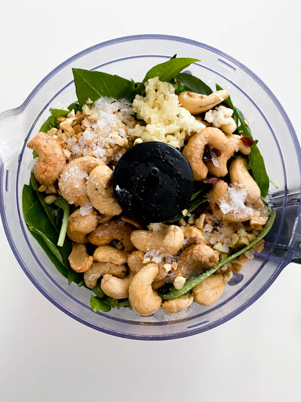 The cashew nuts, peanuts, garlic, chilli flakes and sea salt are all added to the Thai basil leaves in the bowl of a food processor.