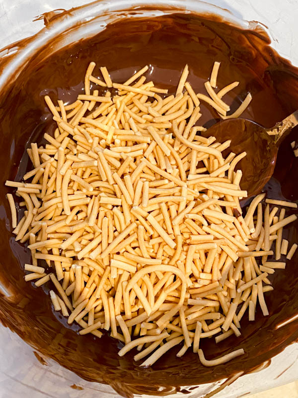 The fried noodles are added to the bowl of melted chcolate.