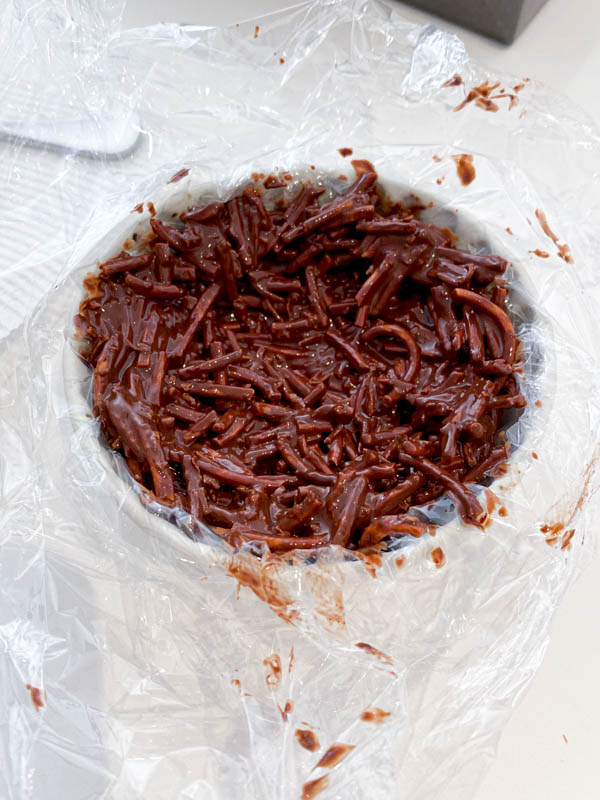 Some of the chocolate nest mixture is moulded into a small bowl that has been lined with cling wrap..