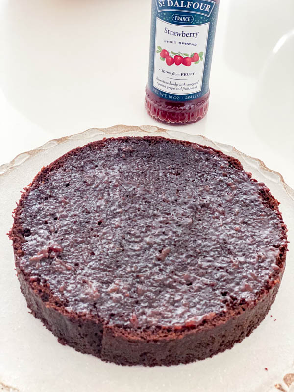 The first layer of chocolate cake is spread with a thin layer of strawberry jam.