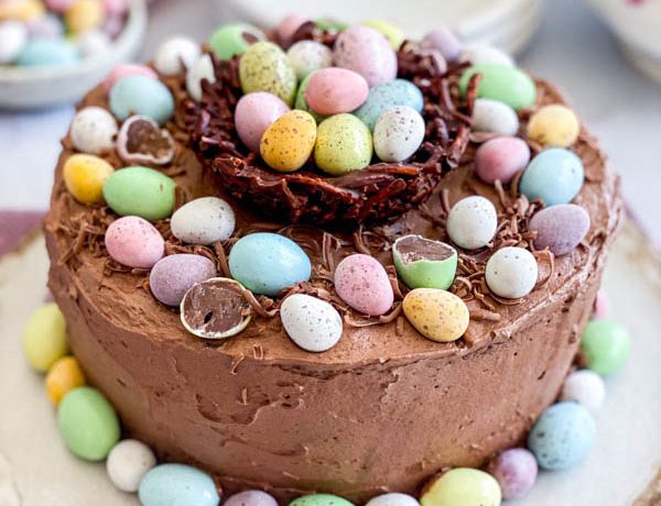 The Easter themed chocolate cake is on a plate on a table with plates and a bowl of mini easter eggs in the background.