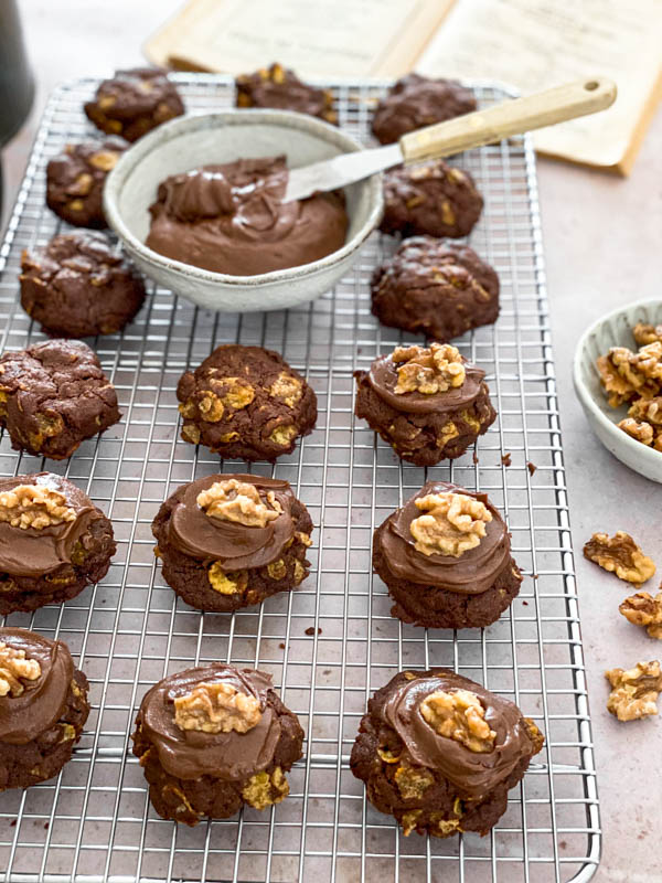 The biscuits are now being iced with chocolate icing and a walnut half is placed on top.