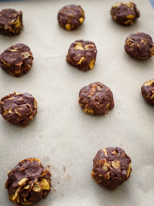 A close up of the mounds of uncooked batter on a baking tray lined with baking paper.