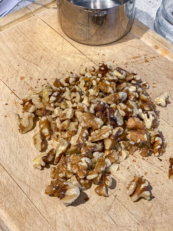 The walnuts have been chopped into pieces and are set aside on a wooden chopping board.