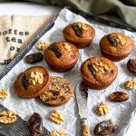 There are five muffins on a decorative tray and one of the muffins is cut open.