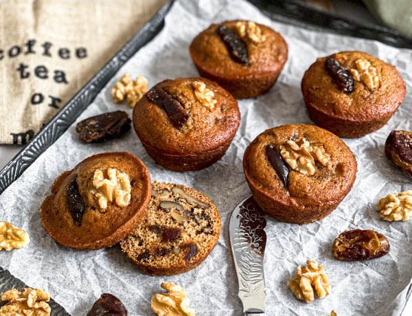 There are five muffins on a decorative tray and one of the muffins is cut open.