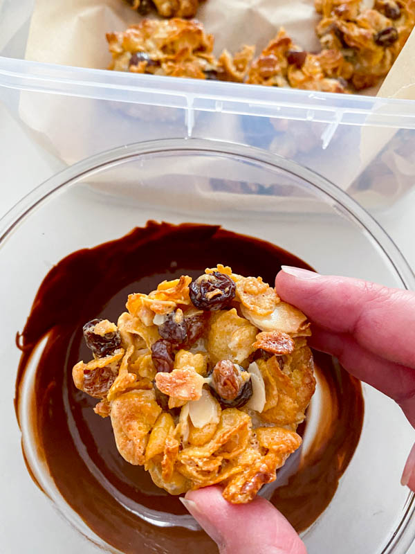 One of the florentines is about to be dunked into a shallow bowl of melted chocolate to coat the underside.