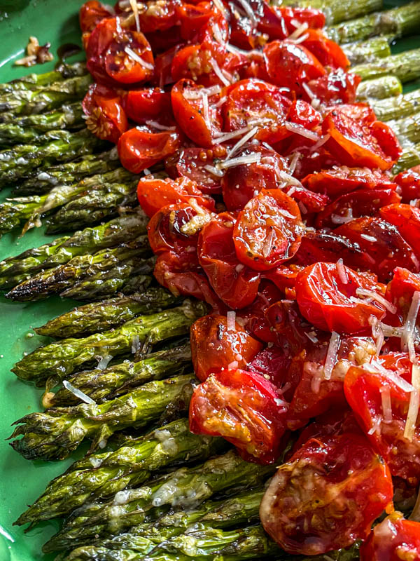 This photo shows a close up of the roasted tomatoes and roasted asparagus on the plate. The ends of the asparagus and parts of the tomatoes are slightly charred from roasting.