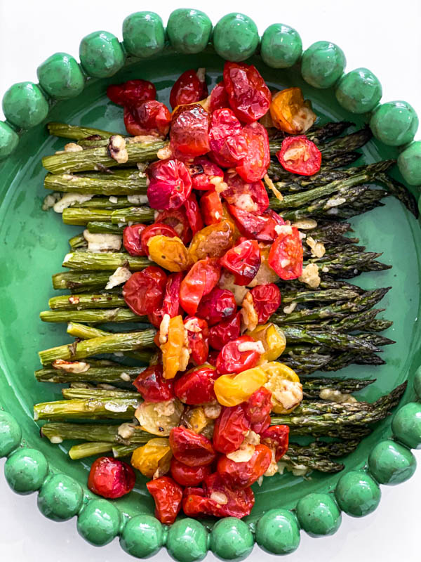 The roasted asparagus is spread out on a green platter with the roasted tomatoes over the top.