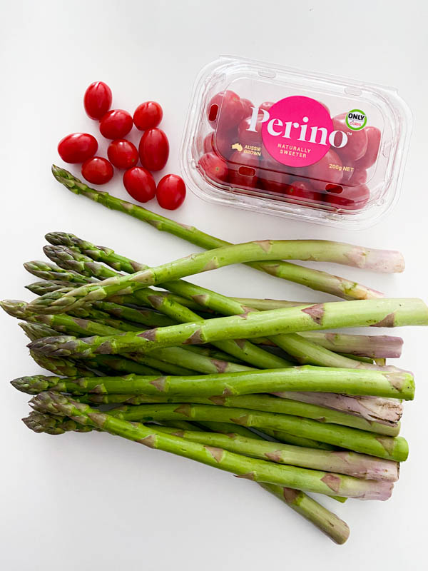 The raw asparagus and baby Roma tomatoes are on a bench ready to be washed.