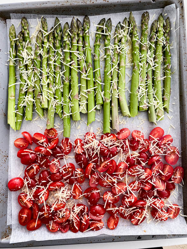 The asparagus and tomato halves are placed on an oven tray in one layer with the asparagus on one side and tomatoes on the other. They have been dressed with olive oil, salt and pepper, and sprinkled liberally with grated parmesan cheese.