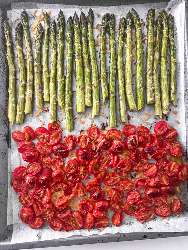 The asparagus and tomatoes have both been roasted and removed from the oven. They are shown here still on the oven tray.